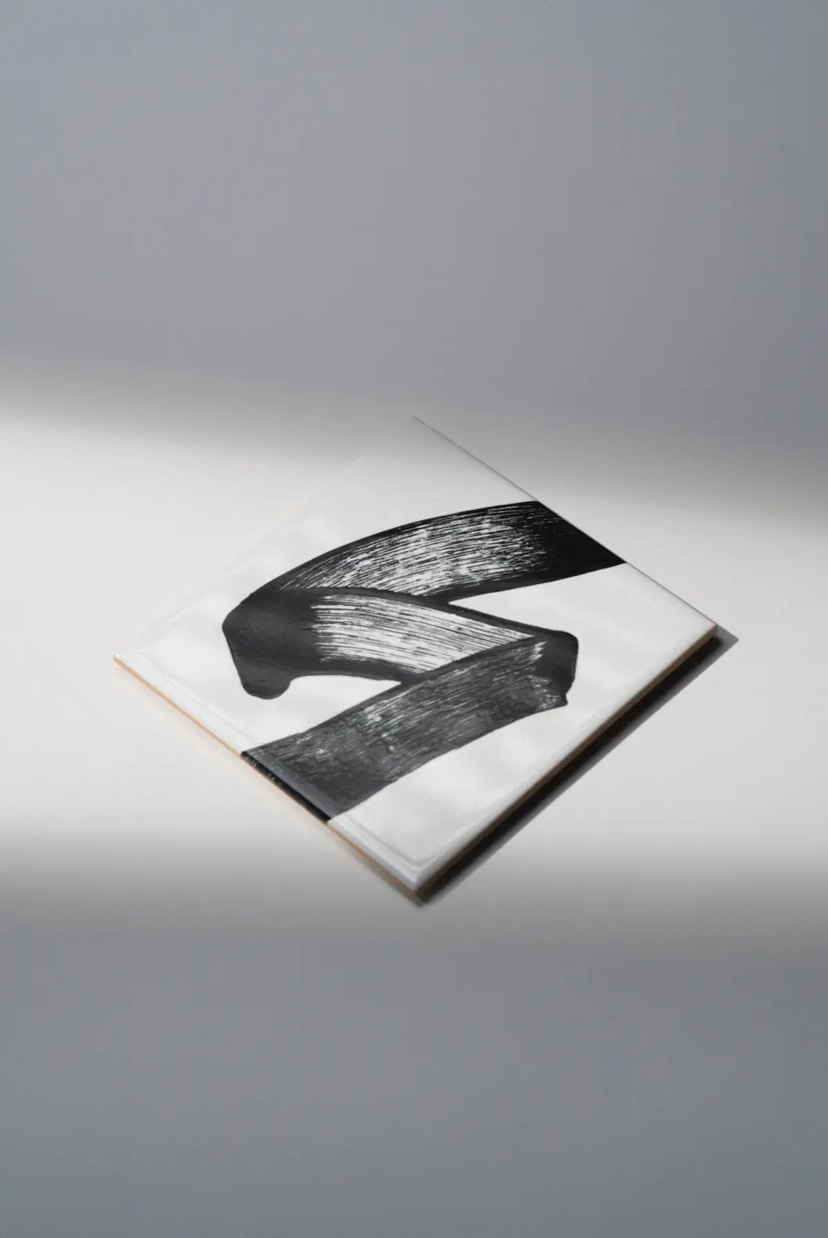 Angled shot of Pattern JonOne ceramic tile by Clay highlighting bold black brushstroke – on sale now at Clay